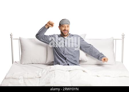 Happy young man with a sleeping mask stretching in a comfortable bed isolated on white background Stock Photo