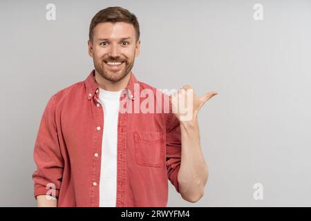 Man points with his thumb to side. Portrait of glad cheerful man demonstrating ad copy space Stock Photo