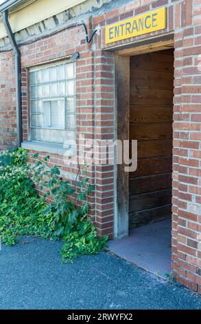 ENTRANCE sign at open door of red brick commercial building shows a dark wood interior. The vintage brick facade has a glass brick wall window. Stock Photo