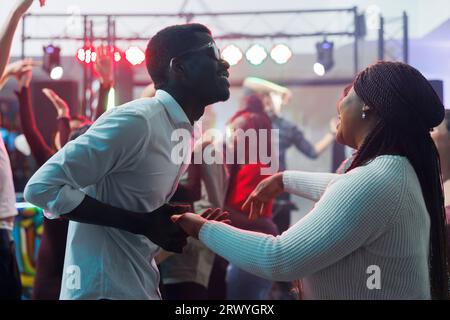 Carefree african american couple dancing together and having fun in nightclub. Cheerful young man and woman clubbers holding hands and partying on dancefloor while clubbing Stock Photo