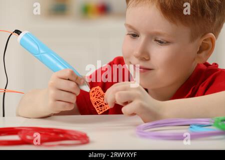 Boy drawing with stylish 3D pen at white table Stock Photo