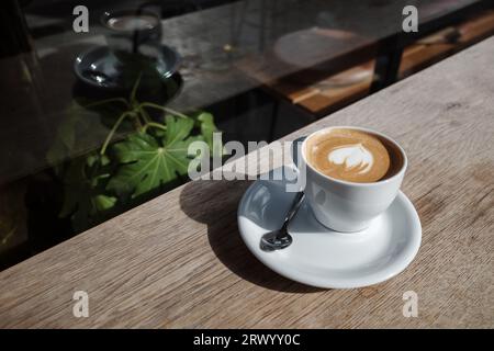 Selected focus and close up view of a white ceramic cup of cappuccino on top with beautiful delicate latte art with heart pattern, on wooden outdoor. Stock Photo