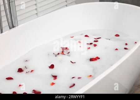 Bathtub filled with foam and rose petals prepared for romantic