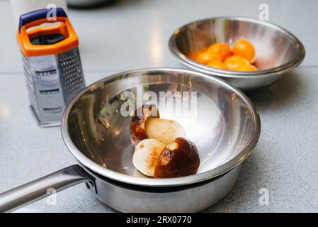 a set of kitchen utensils before cooking, stainless steel bowls, a grater and defrosted porcini mushrooms, a metal frying pan on a kitchen table. Stock Photo