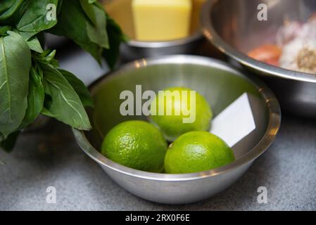 Ingredients for making sauce - lime, basil and butter. a metal bowl filled with limes on top of a counter. Stock Photo