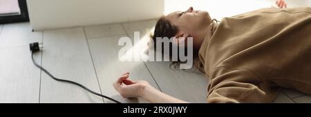 Woman lies on the floor with her eyes closed near electric cable with plug. Stock Photo
