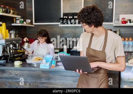 Young guy in an apron with laptop in his hands inside coffee shop cafeteria Stock Photo