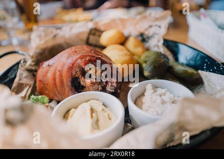 Baked pork shank served with baked potatoes, horseradish, mustard and pickled cucumbers. Traditional Polish dish Stock Photo