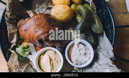 Baked pork shank served with baked potatoes, horseradish, mustard and pickled cucumbers. Traditional Polish dish Stock Photo