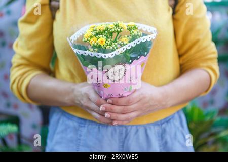 Close-up shot of an unrecognizable woman in a yellow sweater holding a bouquet of yellow flowers Stock Photo