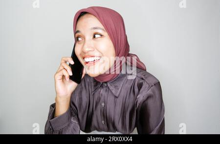 Portrait of happy young muslim woman talking on mobile phone against white background Stock Photo