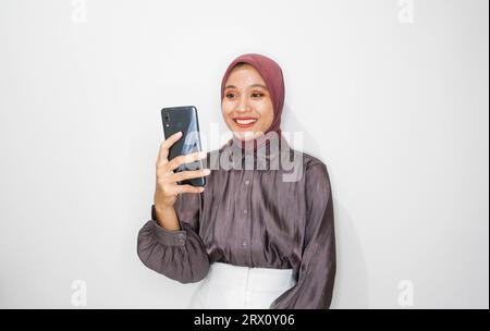 Portrait of happy young muslim woman talking on mobile phone against white background Stock Photo