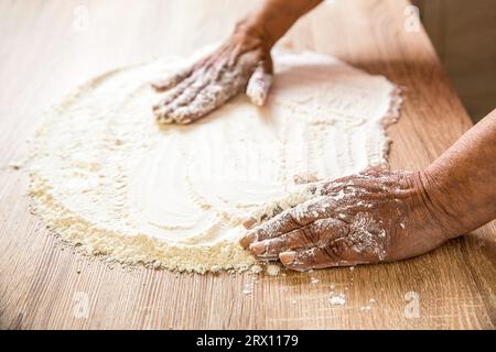 Women's hands, flour and dough. Woman preparing dough for home baking. Dough on white powder covered table. Hand flour. Hands baker with flour in Stock Photo