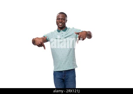 young handsome african guy with short haircut dressed in a mint t-shirt and jeans shows his hands down to the advertising space Stock Photo