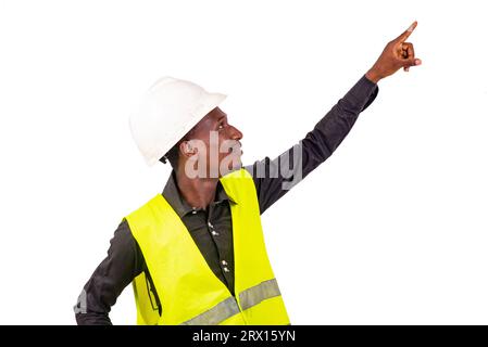 young male construction engineer wearing vest and white safety helmet and pointing finger aside while smiling. Stock Photo