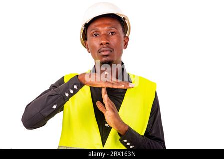 Young tired engineer man wearing green vest and white safety helmet while making pause gesture. Stock Photo