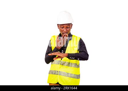 Young astonished engineer man wearing green vest and white safety helmet while checking the time on the wrist watch. Stock Photo