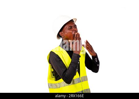 Young tired engineer man wearing green vest and white safety helmet while yawning with hand over mouth. Stock Photo