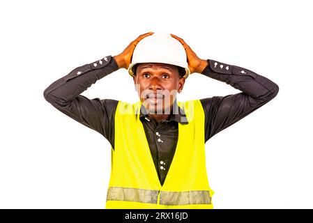 young man engineer wearing green vest and safety helmet while holding head with both hands. Stock Photo