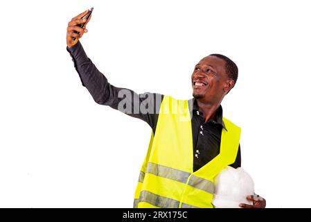 young man engineer wearing green vest and safety helmet while taking photos on mobile phone smiling. Stock Photo