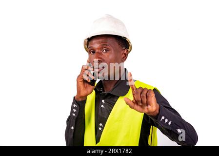 young busy engineer man wearing green vest and hard hat and talking on mobile phone while showing waiting gesture with raised index finger. Stock Photo