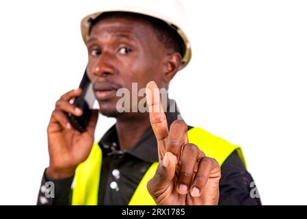 young busy engineer man wearing green vest and hard hat and talking on mobile phone while showing waiting gesture with raised index finger. Stock Photo