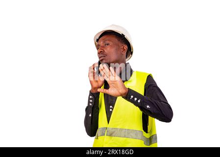 a construction engineer with safety helmet standing on white background talking on the cell phone making stop gesture. Stock Photo
