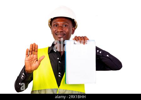 young man inspector architect wearing green vest and holding clipboard while making stop gesture with palm smiling. Stock Photo