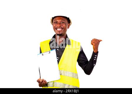 young man inspector architect wearing green vest and holding clipboard while pointing thumb aside smiling. Stock Photo