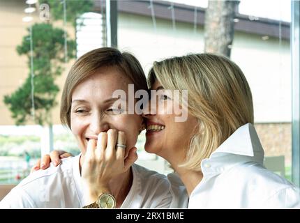 two cute women, 35-40 years old, sharing secrets in a cafe, on a Stock Photo