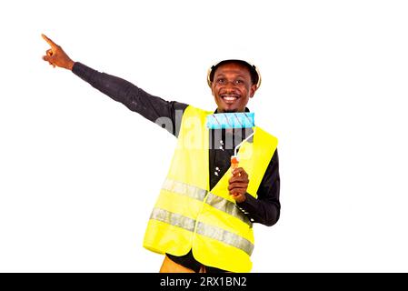 young painter man wearing green vest and holding brush roll and pointing index finger aside smiling. Stock Photo