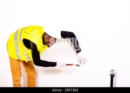 young happy carpenter man wearing white glove and pointing at wall with hammer while smiling. Stock Photo