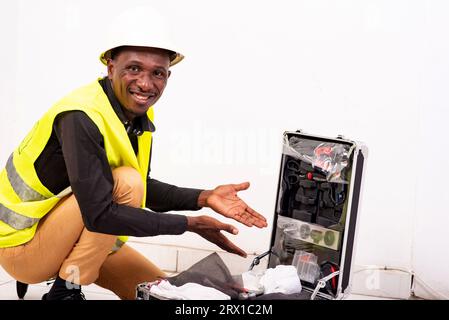 young man engineer wearing safety vest and helmet showing box with tools while smiling. Stock Photo