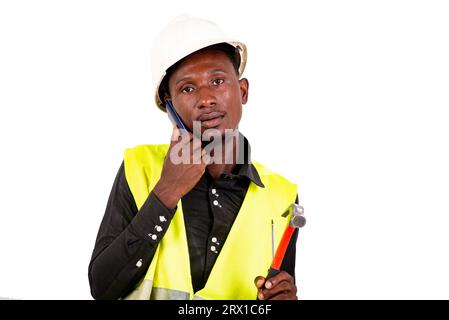 young man technician wearing green vest and safety helmet and holding tools in hands and talking on mobile phone. Stock Photo