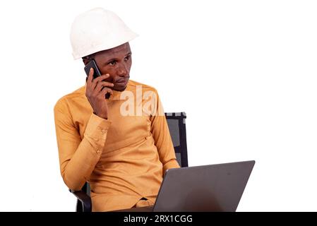 young business man engineer wearing hard hat talking on mobile phone while working with laptop. Stock Photo