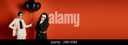 woman in sugar skull makeup and white suit with black balloons near spooky man on red, banner Stock Photo