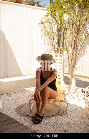 Woman in Straw Hat Sitting on Pool Lounge Chair Stock Photo