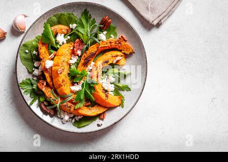 Autumn salad with grilled pumpkin, goat cheese, pecan nuts and herbs on white background. Seasonal autumn warm salad recipe, vegetarian food. Stock Photo