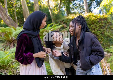 Horizontal photo of a Muslim young woman and african american female friends laughing in a park Stock Photo