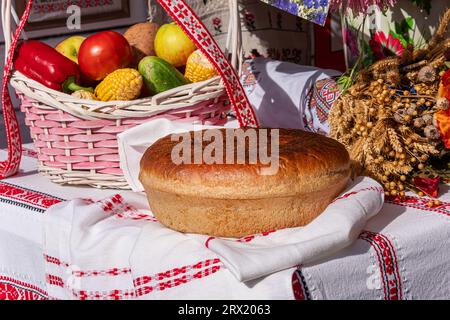 bread, fresh vegetables in a basket and a bouquet of dried flowers on the table with a white tablecloth. Stock Photo