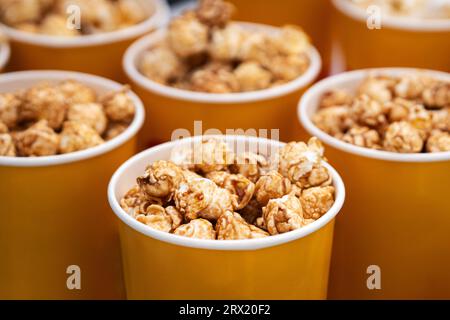 Paper bucket with popcorn, concept of watching TV or cinema. delicious sweet caramel brown popcorn. in a yellow orange glass close-up. boxes of popcor Stock Photo