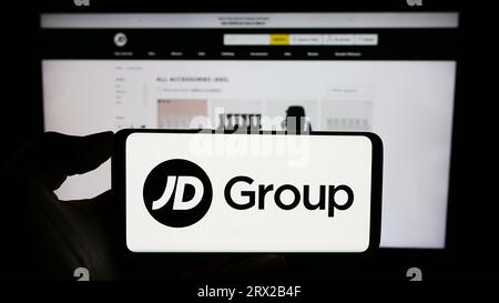 Person holding cellphone with logo of British retail company JD Sports Fashion plc on screen in front of webpage. Focus on phone display. Stock Photo