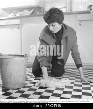 Cleaning in the 50s. A woman washes the floor with a scrub brush. The pattern on the kitchen floor is period-typical checkered in the colors white and black. Sweden 1956. Kristoffersson ref BX62-5 Stock Photo