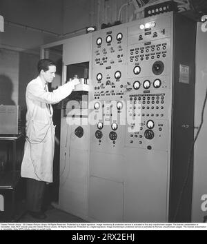 Man and machine in the 1940s. An engineer dressed in a white coat at an appliance with a control panel where there are a variety of sockets, knobs, controls and gauges. Some of the technical equipment is visible such as transistors and technical components. The function of the device or what is measured is unknown. Sweden 1943. Kristoffersson ref AH23-9 Stock Photo