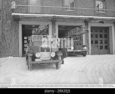 In the 1940s Firemen from the Kungsholmen fire station in Stockholm rush out in their open fire truck. Dressed in fire uniforms and helmets with emblems, they drive out of the fire station. The fire engine is equipped with ladders and a pump equipment. A brass bell sounds the alarm during the call. February 1940. Kristoffersson ref 57-4 Stock Photo