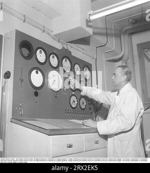 Man and machine in the 1950s. An engineer dressed in a white coat at an appliance with a control panel where there are a variety of sockets, knobs, controls and gauges. The function of the device or what is measured is unknown. Sweden 1950. Kristoffersson ref BB69-8 Stock Photo