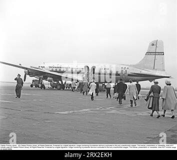 Airline passengers in the 1950s. A four-engine passenger aircraft of the type SE-BDM Douglas DC-6-477B Cloudmaster from the Scandinavian airline SAS is lined up at a Swedish airport and the air passengers have started to go up the stairs and board the aircraft. The weather is a bit gray and dull and one can speculate that the Swedes who have started traveling on charter trips to southern Europe may be on their way to where it is sunny and warm and thus avoid the dreary weather. Sweden 1952. Kristoffersson ref BG60-4 Stock Photo