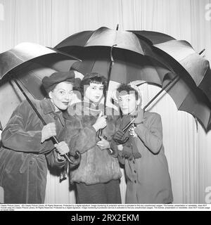 Three women under umbrellas in the 1950s. The actor Harriet Andersson in the middle with Mary Rapp on the left, stands with a third revue actress under each umbrella in connection with a revue. Sweden 1952. Kristoffersson ref BK100-11 Stock Photo
