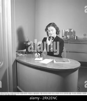 Woman in the 1940s. Interior of an office where a young woman sits at a desk and talks on the phone. She is neatly dressed and taking notes while talking on the phone. Sweden 1945. Kristoffersson ref M107-2 Stock Photo