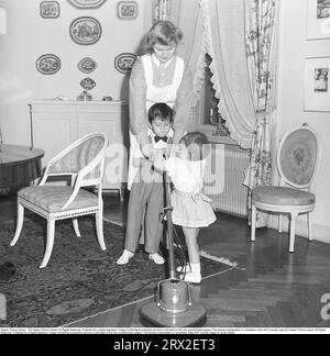 Cleaning in the past. A young woman employed as a nanny and domestic help stands in the living room with the family's two children. She tries to tidy up the parquet floor, but the children really want to help with the work. She uses a floor polisher that polishes and polishes the floor in connection with applying floor wax. Sweden 1946. Kristoffersson ref X147-1 Stock Photo